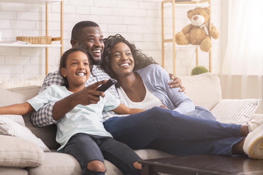Happy african american family relaxing and watching tv at home, enjoying weekend together.
