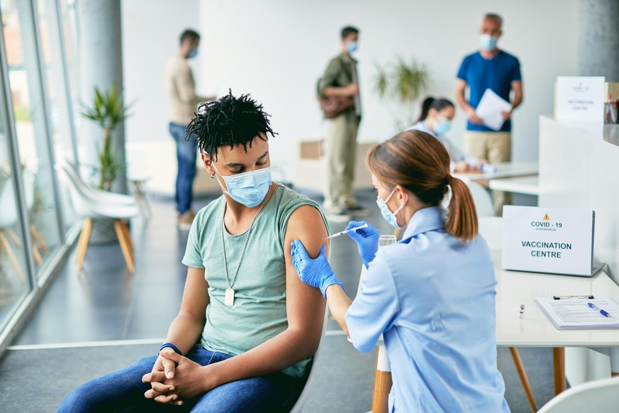 Young black man receiving COVID-19 vaccine during immunization at vaccination center.