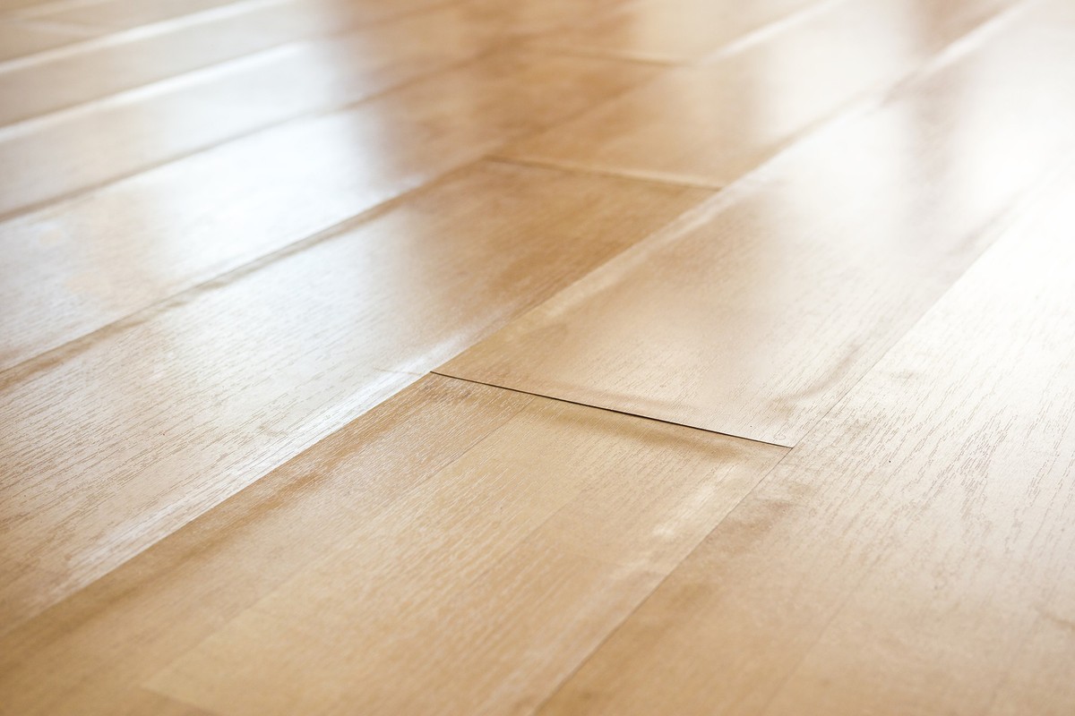 Close up of light beige swollen laminate boards with buckling edge pieces. Floor damage texture. Selective focus in center.