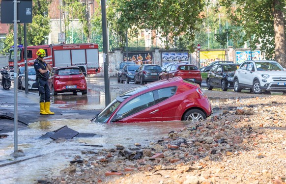 30.09.2023, Italien, Mailand: Ein Feuerwehrmann steht vor einem Auto, das nach einem Wasserrohrbruch in ein mit Wasser überflutetes Loch gerutscht ist. Der Wasserrohrbruch auf der Piazza Bettini / Eck ...