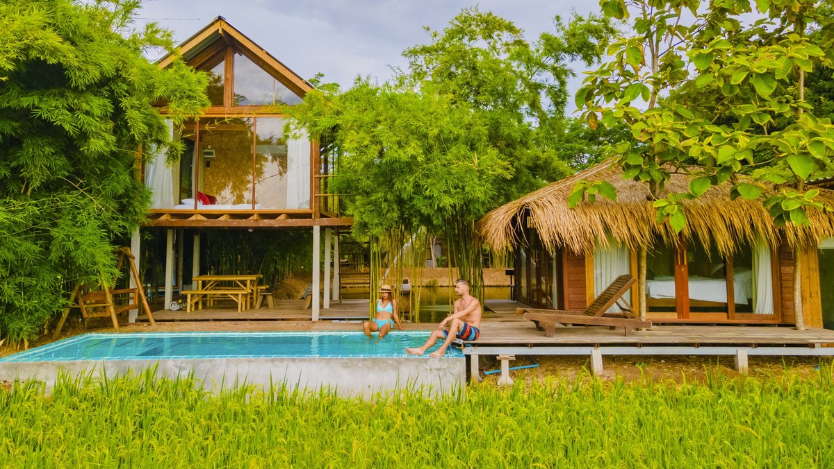 a couple of men and women in front of a Bamboo hut homestay farm, with Green rice paddy fields in Central Thailand with a small plunge pool