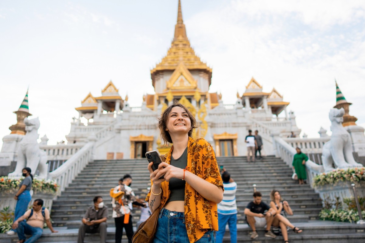 Woman using smartphone standing on the background of Wat Traimit during her vacation in Bangkok