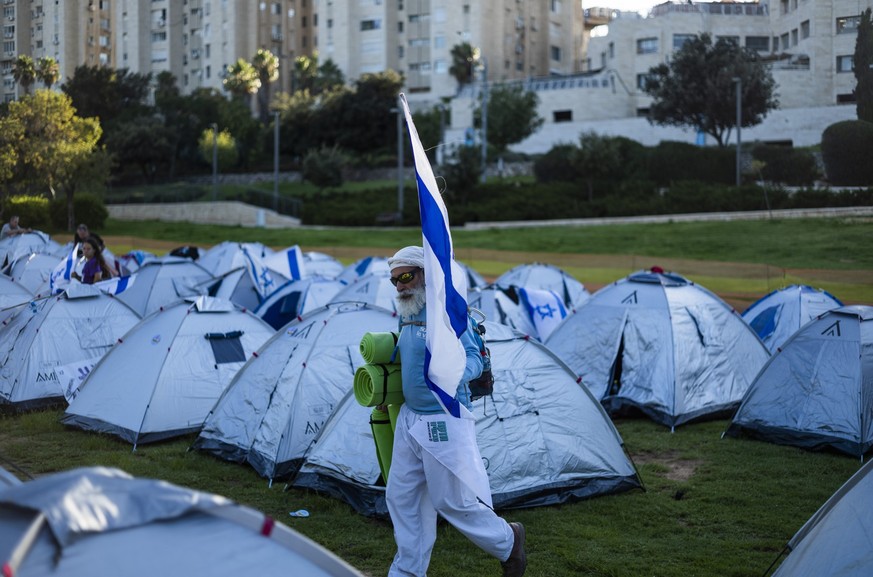 23.07.2023, Israel, Jerusalem: Ein Demonstrant geht neben Zelten. Demonstranten, die die letzte Etappe eines viertägigen, 70 Kilometer langen Marsches von Tel Aviv aus absolviert haben, campieren vor  ...