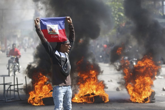 01.03.2024, Haiti, Port-au-Prince: Ein Demonstrant hält eine haitianische Flagge während Protesten für den Rücktritt von Premierminister Henry hoch. Foto: Odelyn Joseph/AP +++ dpa-Bildfunk +++