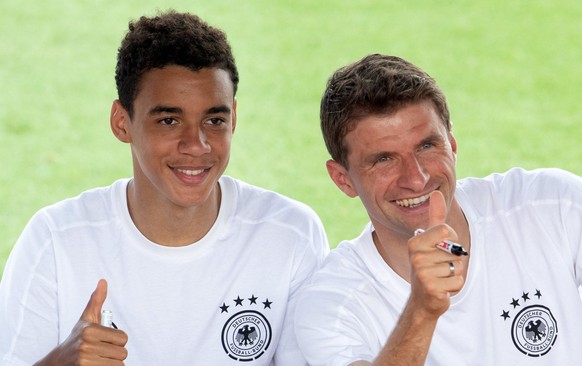 ARCHIV - 26.06.2021, Bayern, Herzogenaurach: Fußball: EM, Autogrammstunde der deutschen Nationalmannschaft auf dem Adi-Dassler-Sportplatz. Deutschlands Jamal Musiala (l) und Thomas Müller grüßen Fans  ...