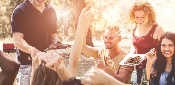 Happy multiracial friends eating, drinking beer and laughing together at barbecue dinner - Young happy people having fun at bbq meal - Friendship and food concept - Focus on guys faces