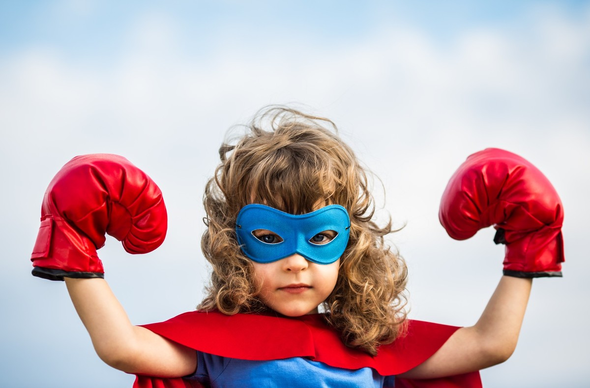 Superhero kid wearing boxing gloves against blue sky background. Girl power and feminism concept