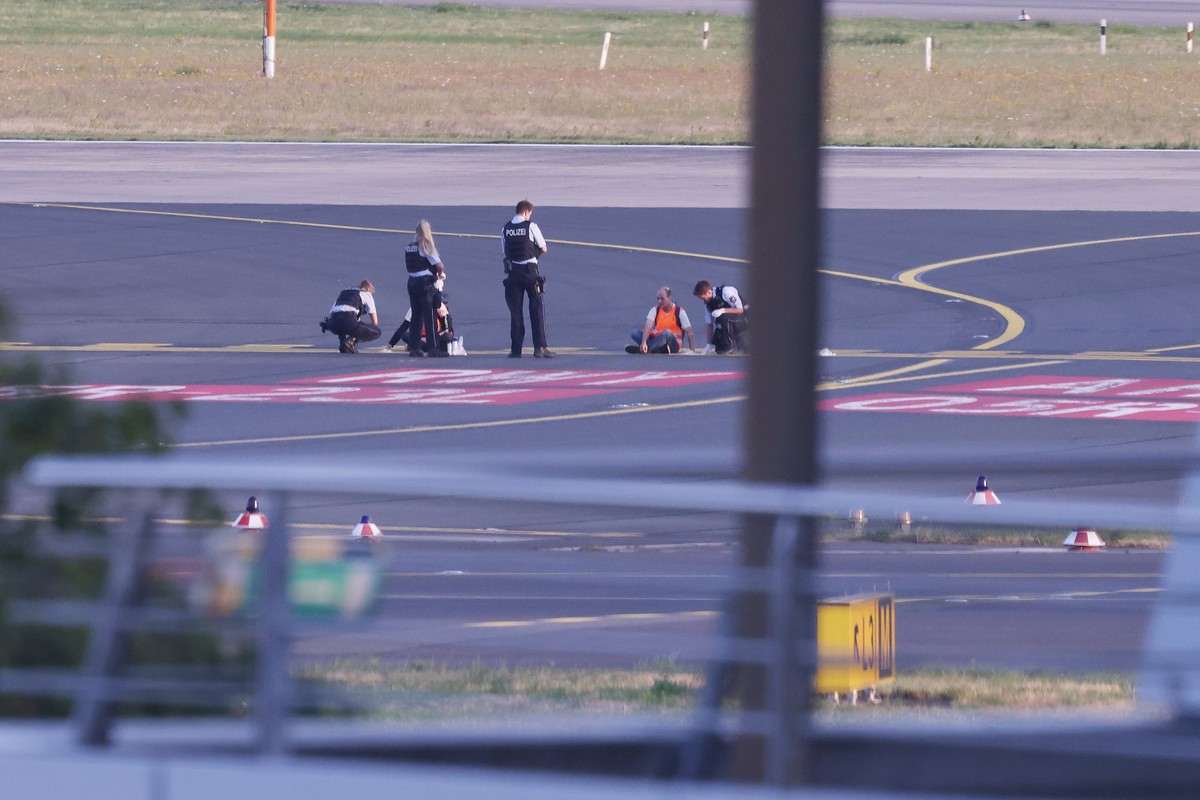 ARCHIV - 13.07.2023, Nordrhein-Westfalen, Düsseldorf: Polizisten stehen auf dem Flugfeld und versuchen Aktivisten der Gruppe Letzte Generation am Flughafen vom Asphalt zu lösen, nachdem sie sich festg ...