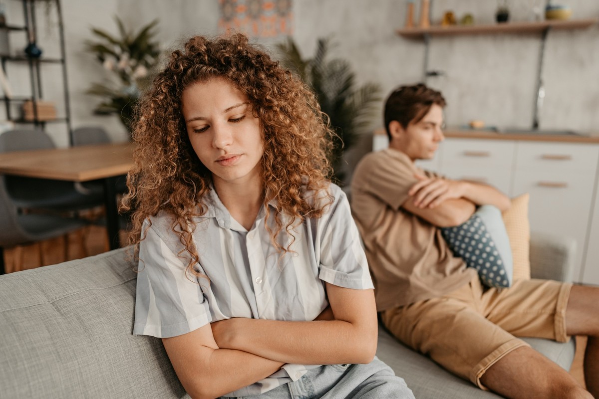 Young couple with relationship problems, sitting on the sofa in the living room and arguing.