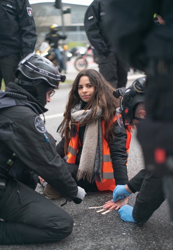 Die Polizist:innen versuchen Lea von der Straße zu lösen, die sich mit Sekundenkleber festgeklebt hat.