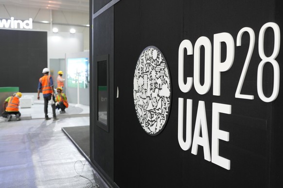 29.11.2023, Vereinigte Arabische Emirate, Dubai: Arbeiter bauen vor dem Beginn der Weltklimakonferenz COP28 in der Nähe eines Logos des UN-Klimagipfels Stände auf. Bei dem COP28-Treffen wollen mehr al ...