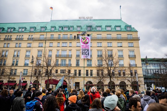 13.04.2023, Berlin: Aktivisten der Klimagruppe «Extinction Rebellion» stehen am Ende einer Demonstration auf einer Balustrade des Hotel Adlon mit einem Banner und gezündeter Pyrotechnik. Auf dem Banne ...