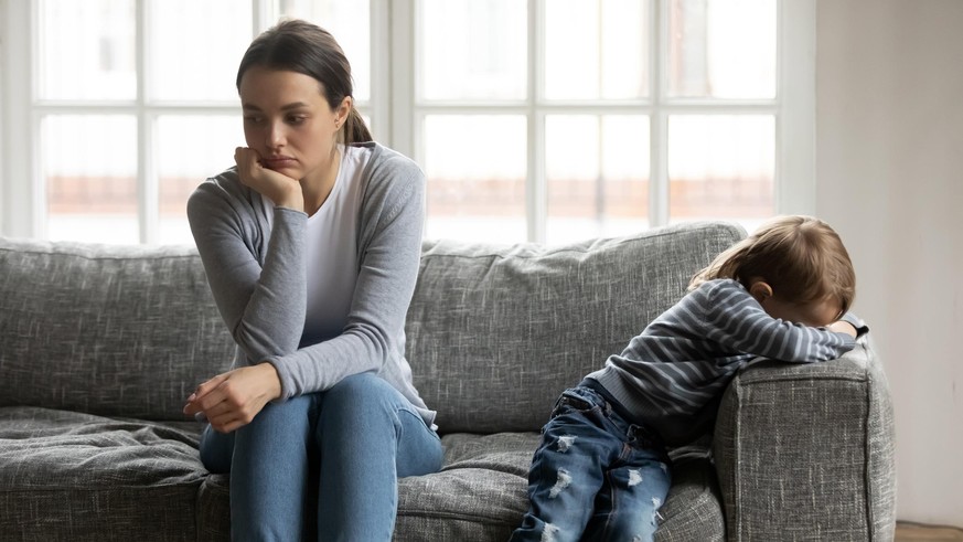 Stressed young mommy sitting separate on couch with offended crying little preschool kid boy, dissatisfied with disrespectful attitude, generations gap, family relationship problems concept.