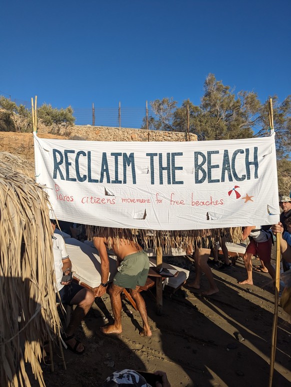 HANDOUT - 02.08.2023, Griechenland, -: &quot;Reclaim the beach&quot; steht auf einem Banner an einem Strand auf der Kykladen-Insel Paros. Ein paar Dutzend Bürger der Insel Paros könnten zum Vorreiter  ...