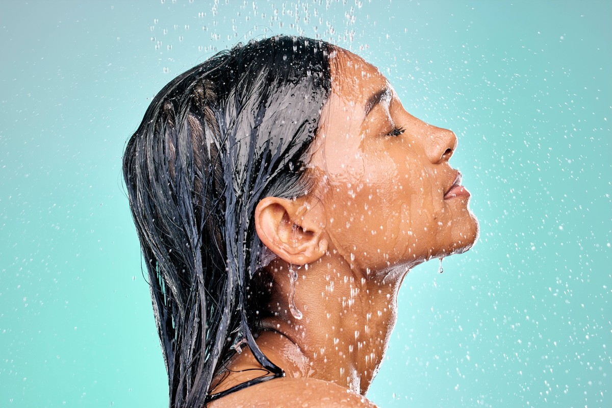 Studio, shower and face of woman for skincare with wellness, morning routine and safety from bacteria. Dermatology, water drops and Indian girl with facial cleaning for skin health by blue background. ...