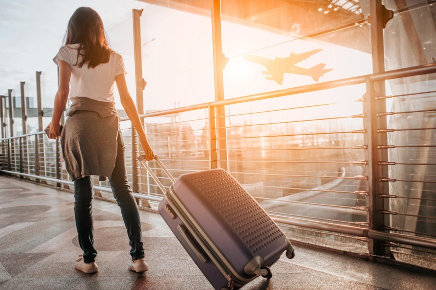 Young woman pulling suitcase in airport terminal. Copy space