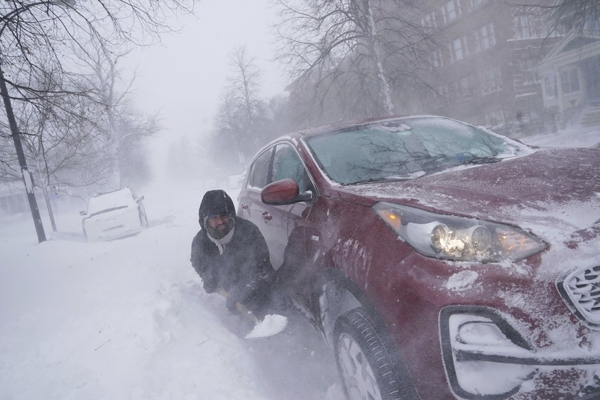 24.12.2022, USA, Buffalo: Gamaliel Vega versucht, sein Auto auf der Lafayette Avenue auszugraben, nachdem er etwa einen Block von seinem Haus entfernt in einer Schneewehe stecken geblieben ist, währen ...