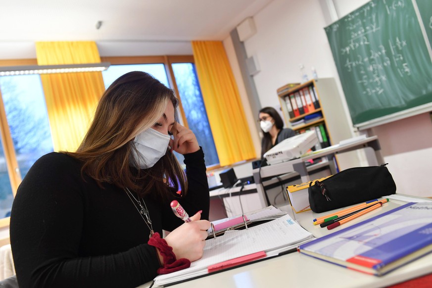 Schulunterricht in Zeiten der Coronavirus Pandemie. Lehrerin sitzt an ihrem Schreibtisch-eine Schuelerin sitzt auf ihrem Platz und lauscht dem Unterricht,konzentriert sich und denkt nach, Konzentratio ...