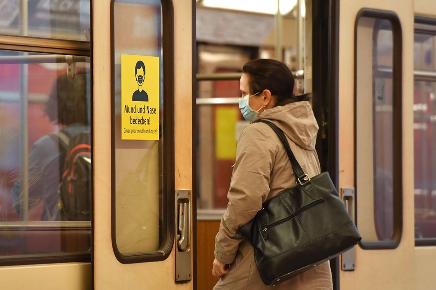 Maskenpflicht im oeffentlichen Personennahverkehr ab dem 27.April. U-Bahn Muenchen,Messestadt West. Ein Fahrgast,Frau mit Mund-Nasen-Schutz steigt in einen U-Bahn Zug ein. An der Tuer haengt ein Hinwe ...