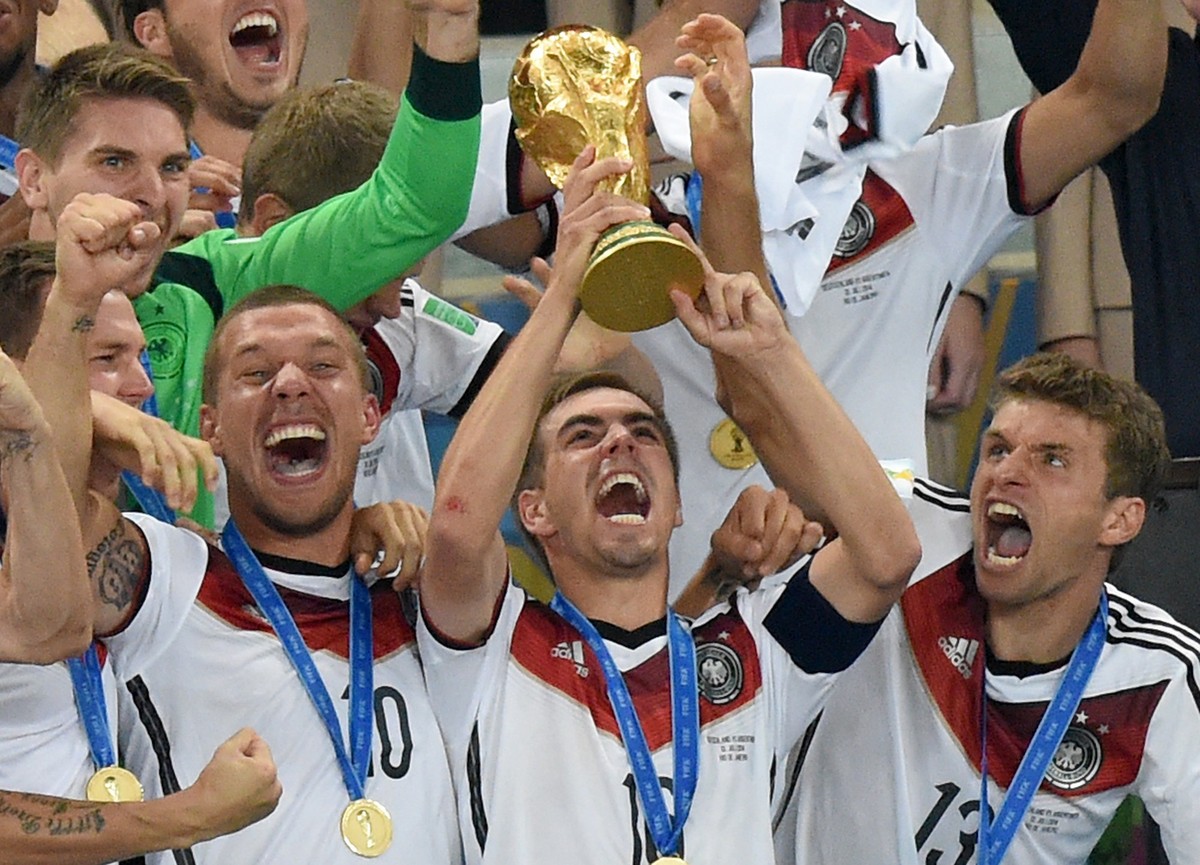 ARCHIV - 12.07.2014, Brasilien, Rio de Janeiro: Philipp Lahm (M) aus Deutschland jubelt am 13.07.2014 mit dem WM-Pokal zwischen seinen Teamkollegen Lukas Podolski (l) und Thomas Müller (r) während der ...