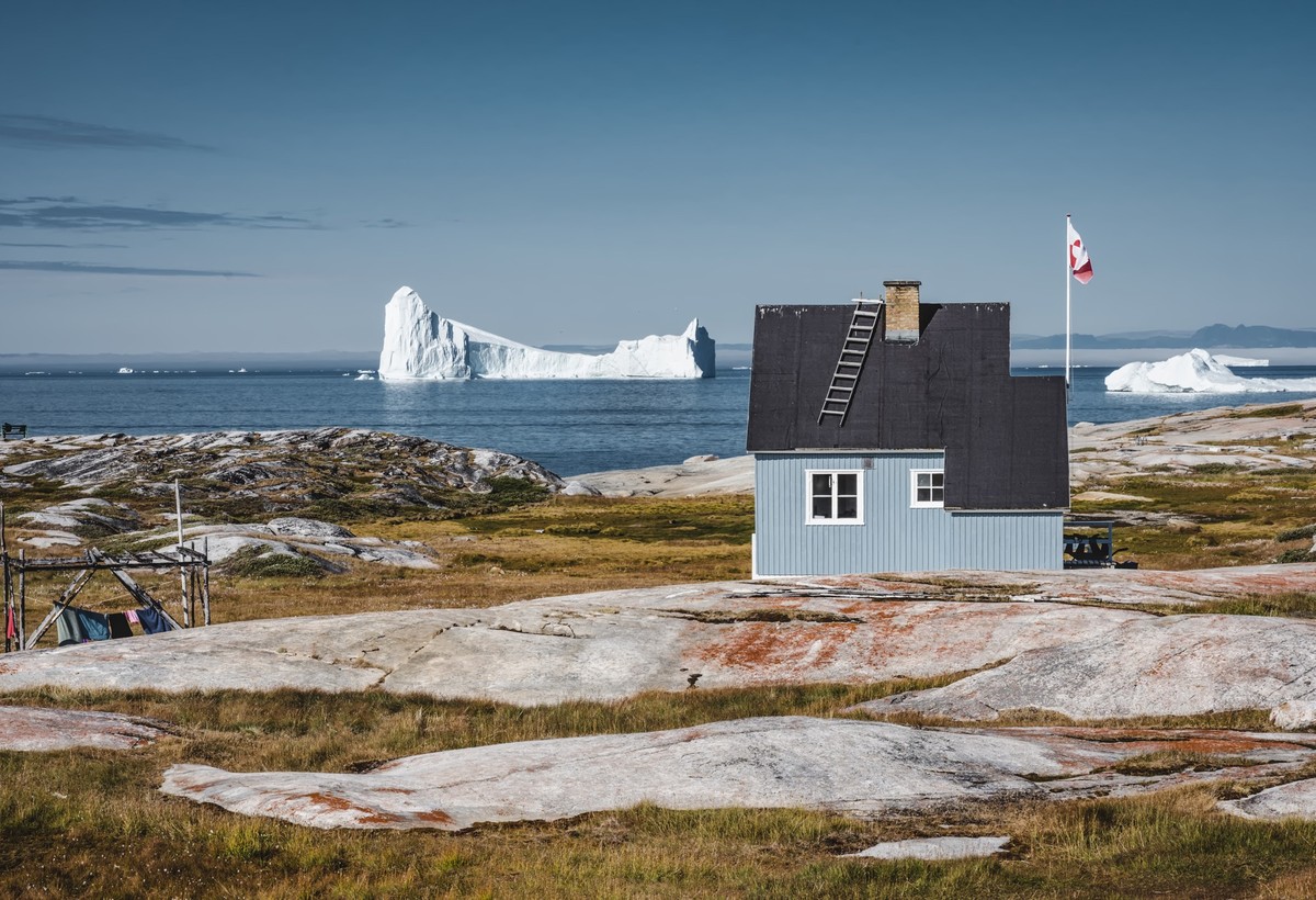 Typical wooden colourful fisher house with iceberg in Qeqertarsuaq, Disko bay area Greenland and Ilulissat. Typical architecture in the arctic circle. Summer and blue sky. Photo taken in Greenland.