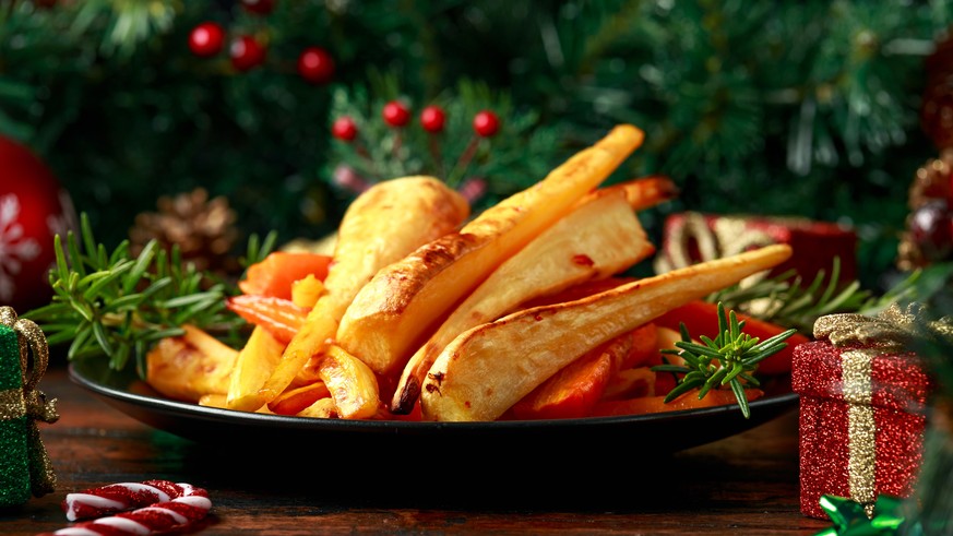 Christmas Roasted Parsnips and Carrots with decoration, gifts, green tree branch on wooden rustic table.