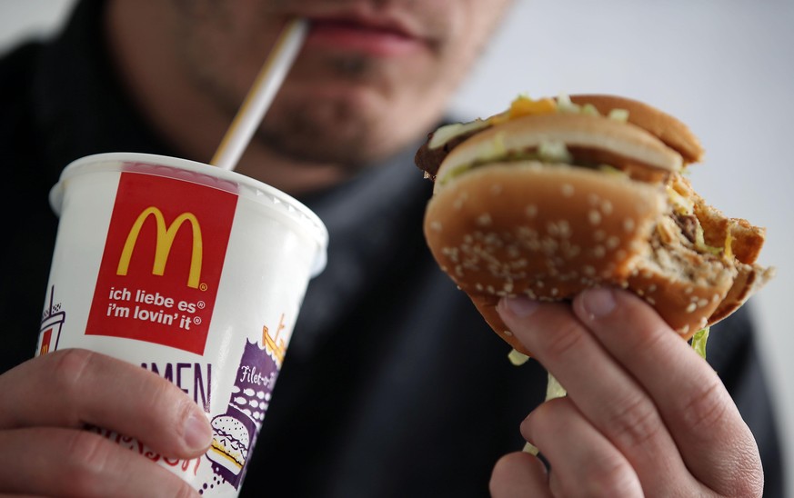 A man drinks a coke and eats a Big Mac burger at a branch of fast food franchise McDonalds in Cologne, Germany, 25 May 2015. Photo: Oliver Berg/dpa