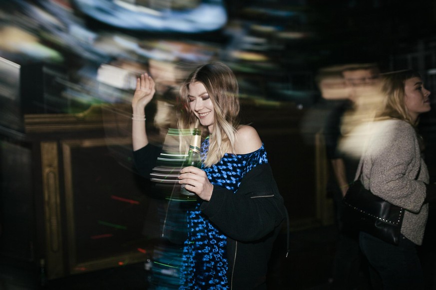 A young woman dancing while drinking a beer at a colourful open air nightclub.