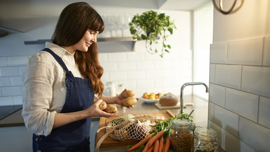 A woman smiles as she unpacks fresh organic vegetables from a plastic free bag in a zero waste kitchen.