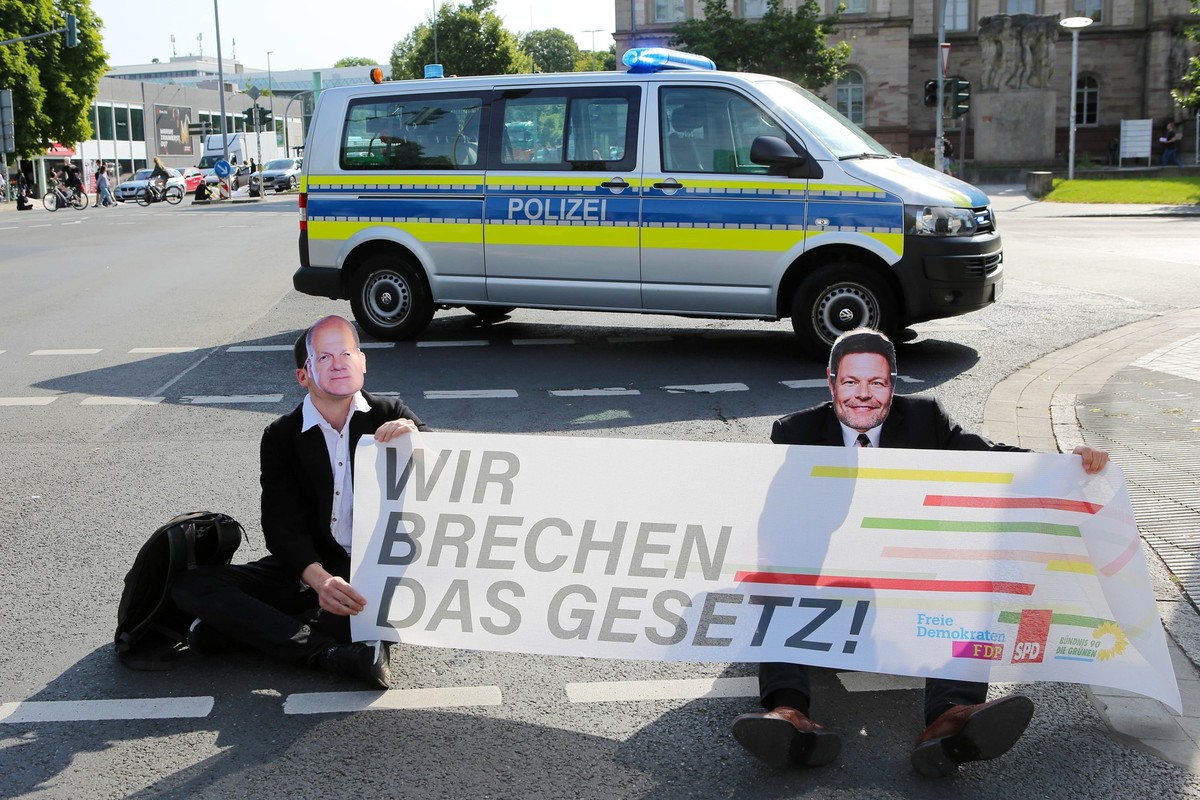 14.07.2023, Niedersachsen, Göttingen: Klimaaktivisten der Gruppe Letzte Generation sitzen mit Masken von Bundeskanzler Scholz (l) und Wirtschaftsminister Habeck bei einer Sitzblockade auf einer Kreuzu ...
