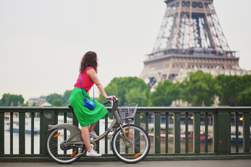 Beauitul young woman in green dress riding a bicycle on a street of Paris, near the Eiffel tower