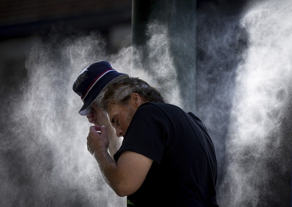 16.08.2023, Kanada, Vancouver: Ein Mann kühlt sich an einer vorübergehenden Nebelstation ab, die die Stadt aufgrund einer Hitzewelle in der Downtown Eastside eingerichtet hat. Der nationale Wetterdien ...