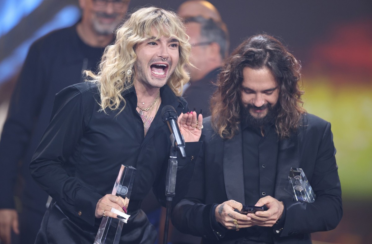 28.09.2023, Nordrhein-Westfalen, K�ln: W�hrend Musiker Bill Kaulitz (l) seinen Fernsehpreis feiert, bedient Bruder Tom Kaulitz (r) sein Smartphone bei der Verleihung ihres ihren Deutschen Fernsehpreis ...