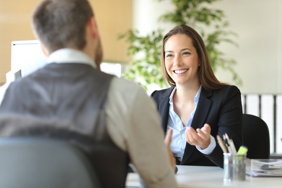 Happy executive coworkers laughing and talking sitting on a desk at the office