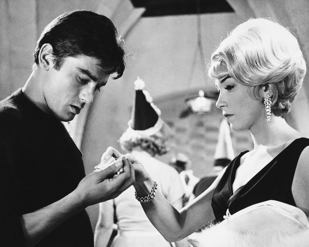 05.08.1964, Großbritannien, Hertfordshire: Die amerikanische Schauspielerin Shirley MacLaine, verkleidet als Gangsterbraut, tupft die Hand ihres französischen Co-Stars Alain Delon am Set des Films &qu ...
