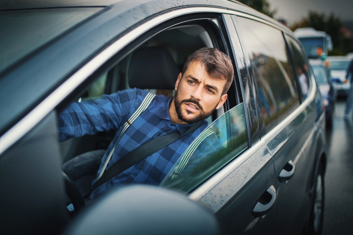 Closeup of a young men stuck in traffic and leaning through the window to see how many vehicles there are in front of him. Staged shot but actual traffic jam.