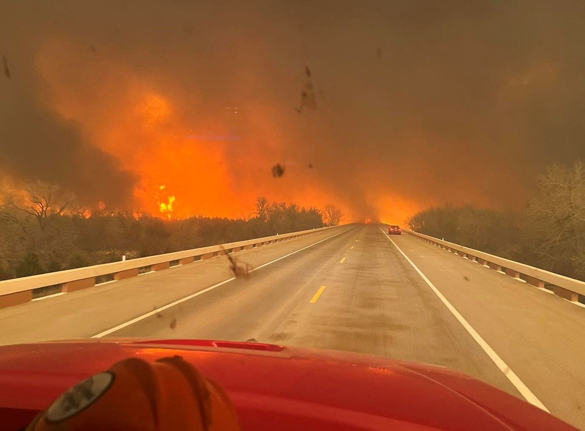 Cars drive as smoke and fire rise from wildfires in a location given as Texas, U.S., in this handout picture released on February 27, 2024. Greenville Fire-Rescue/Handout via REUTERS THIS IMAGE HAS BE ...