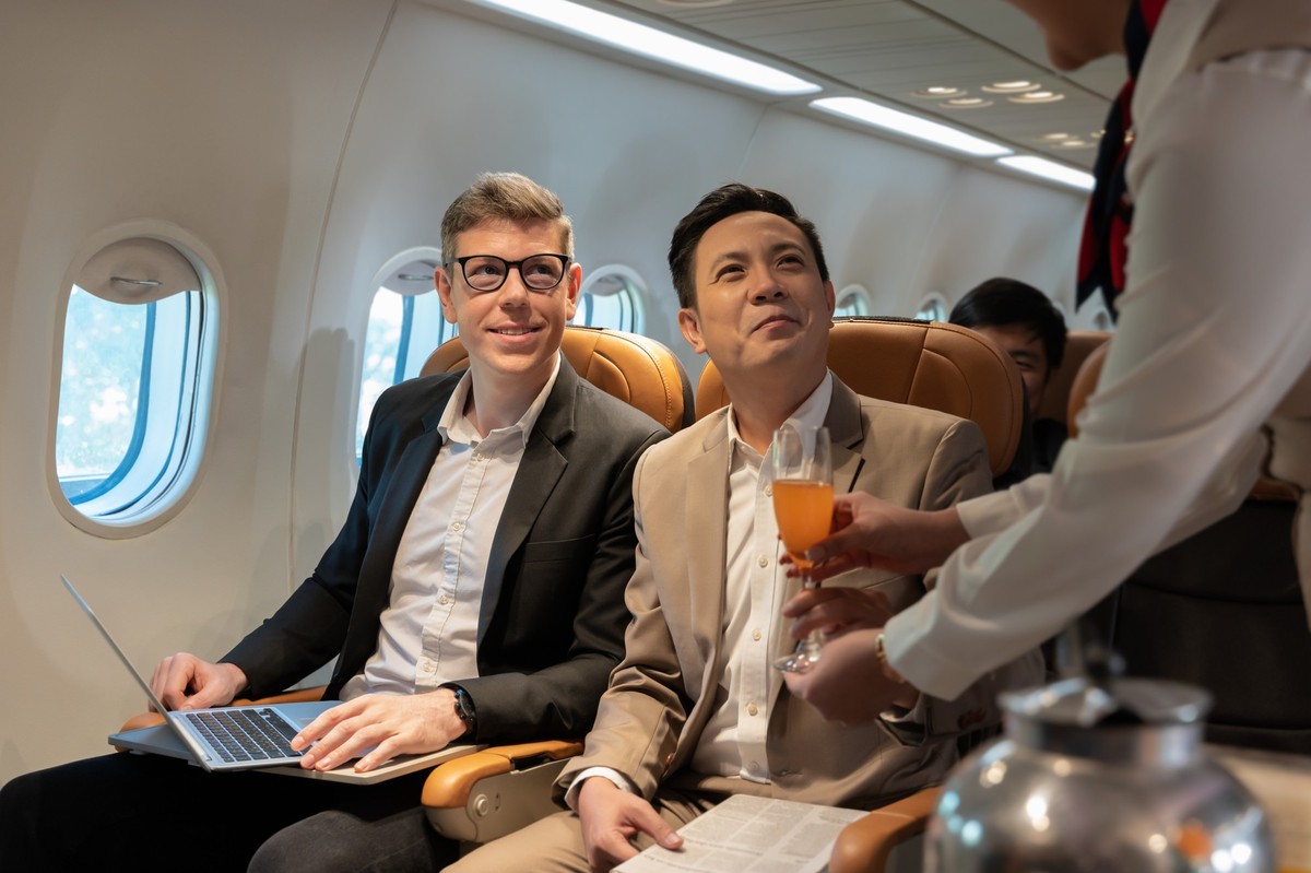 Flight attendant serving orange juice to businessman on plane, In-flight services. Cabin crew service smiling businessman passenger with orange juice on board, In-flight services. Cabin crew service s ...