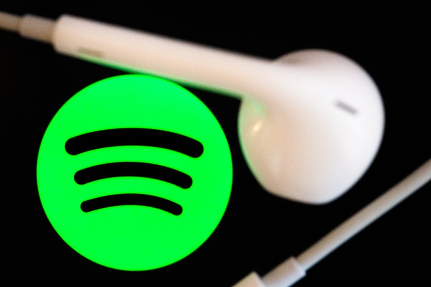 ARCHIV - 07.02.2022, Berlin: Kopfhörer liegen auf dem Bildschirm eines Smartphones, auf dem das Logo vom Musikstreaming-Dienst Spotify angezeigt wird. (zu dpa «Spotify nach 15 Jahren: Musikstreaming-C ...