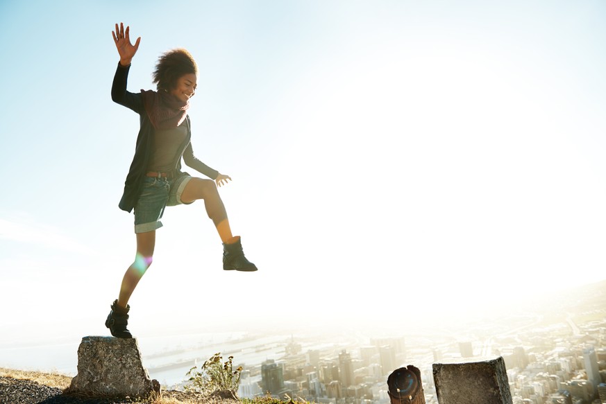 Shot of a young woman jumping from pillar to pillar on the edge of a mountain road