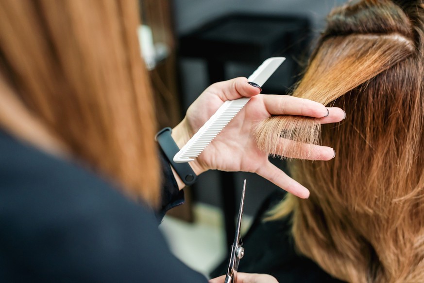 Female hairdresser is holding in hand between fingers a red hair is cutting woman hair close up.