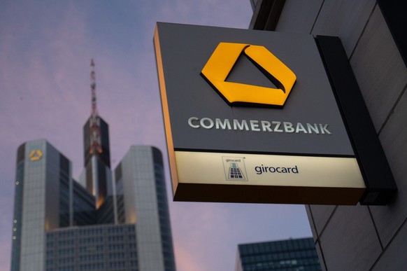 ARCHIV - 13.02.2022, Hessen, Frankfurt/Main: Der Schriftzug �Commerzbank� und das Logo sind auf einem Schild zu sehen. Dahinter ist die Zentrale der Commerzbank zu erkennen. (Zu dpa &quot;Commerzbank- ...