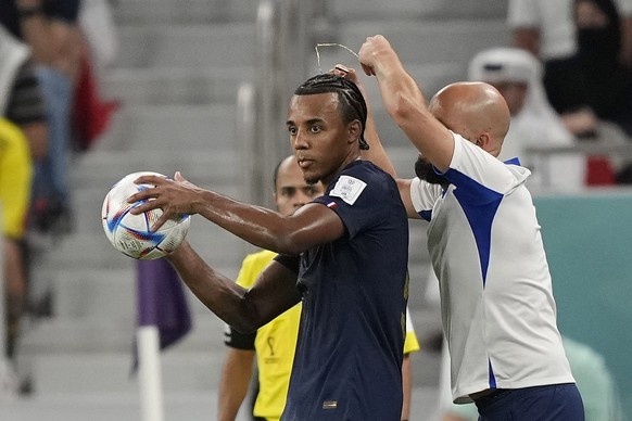 An assistant coach takes of the necklace of France's Jules Kounde during the World Cup round of 16 soccer match between France and Poland, at the Al Thumama Stadium in Doha, Qatar, Sunday, Dec. 4, 202 ...