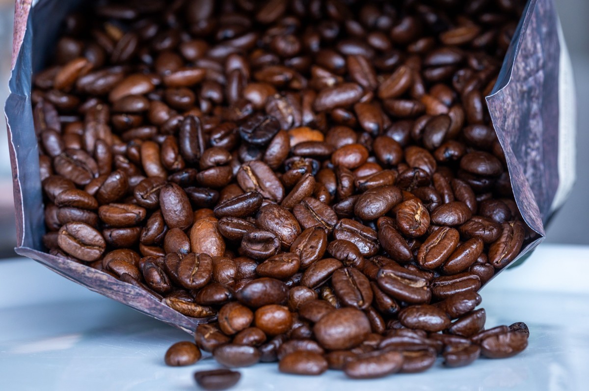 SYMBOLBILD - 02.04.2025, Mecklenburg-Vorpommern, Pokrent: Geröstete Kaffeebohnen liegen vor einer Tüte. (zu dpa: «Handelsverband: Kaffee wird zunehmend weggesperrt») Foto: Jens Büttner/dpa +++ dpa-Bil ...