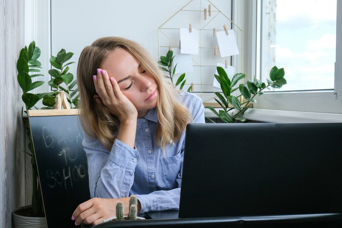 Tired sleepy young caucasian woman worker at desk workplace. Overworking and sleeping deprivation. Businesswoman and Monetary crisis. Freelancer in depression. Sad Woman looking at a laptop at workspa ...