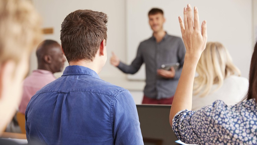 Rear View Of Mature College Student Asking Question In Class ,model released, Symbolfoto,property released PUBLICATIONxINxGERxSUIxAUTxONLY Copyright: xMonkeybusinessx Panthermedia25112392