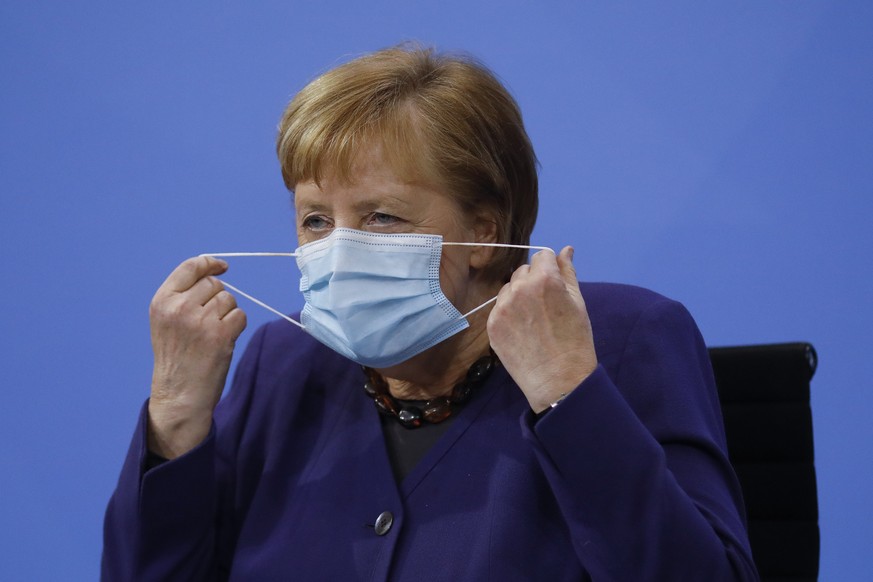 German Chancellor Angela Merkel takes down her face mask as she arrives for a news conference following talks of the government with the federal state governors, at the Chancellery in Berlin, Wednesda ...
