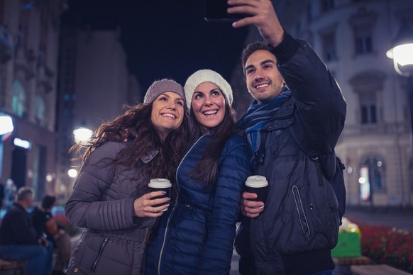 Friends making a selfie with mobile phone, shearing on social media. Outdoors, urban night environment