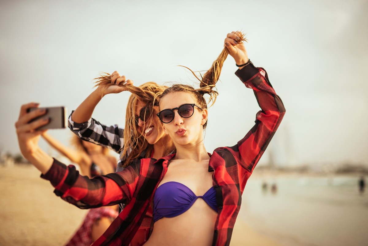 Close up portrait of girls having fun while taking pictures with mobile phone on the beach.