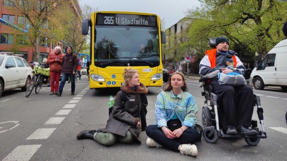 Gunda (Mitte) und andere Klimaaktivist:innen der Letzten Generation blockieren die Durchfahrt eines Linienbusses.